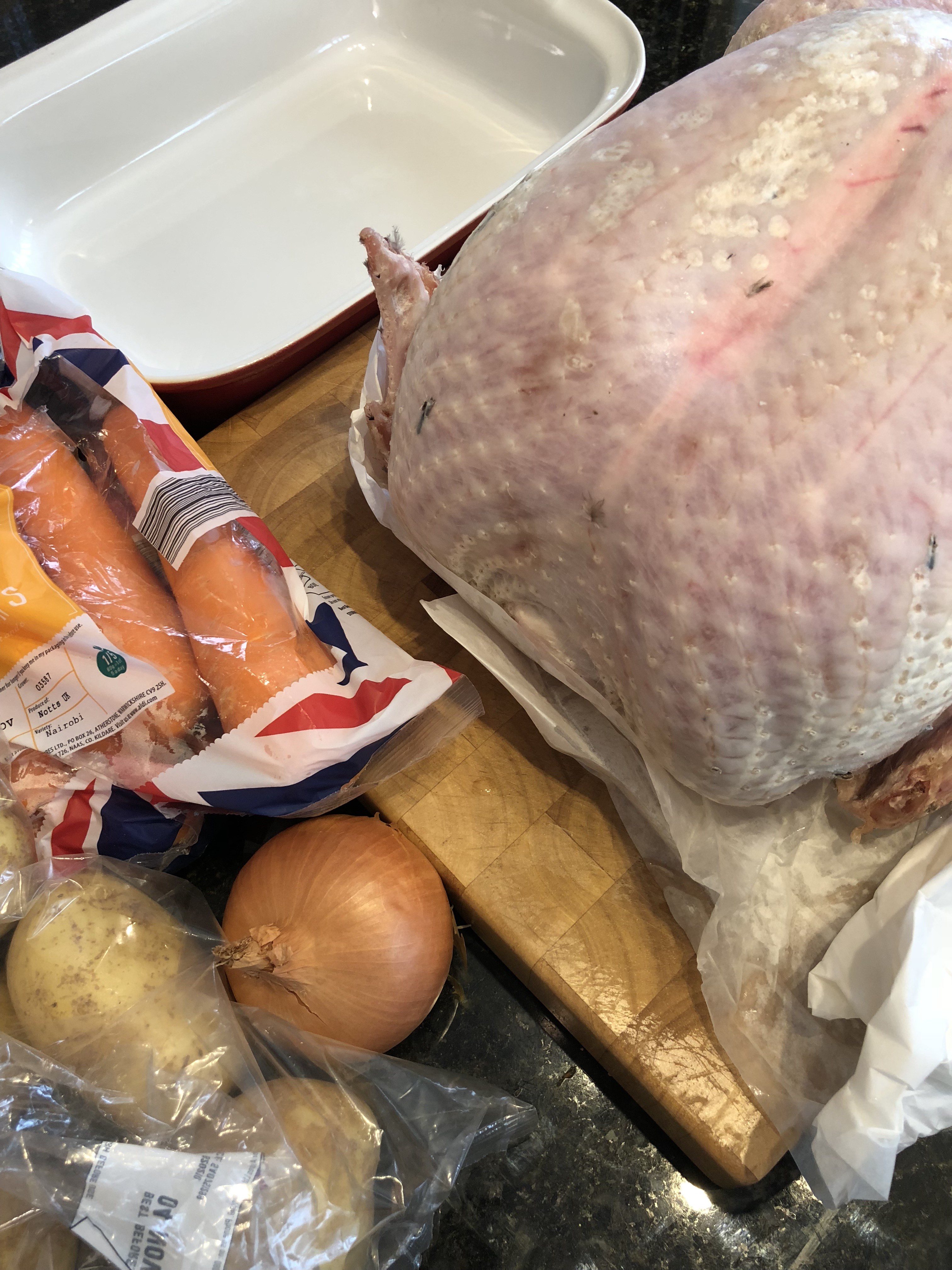 plucked Morton's turkey prepared on wooden chopping block for christmas roast dinner with carrots onions and potatoes