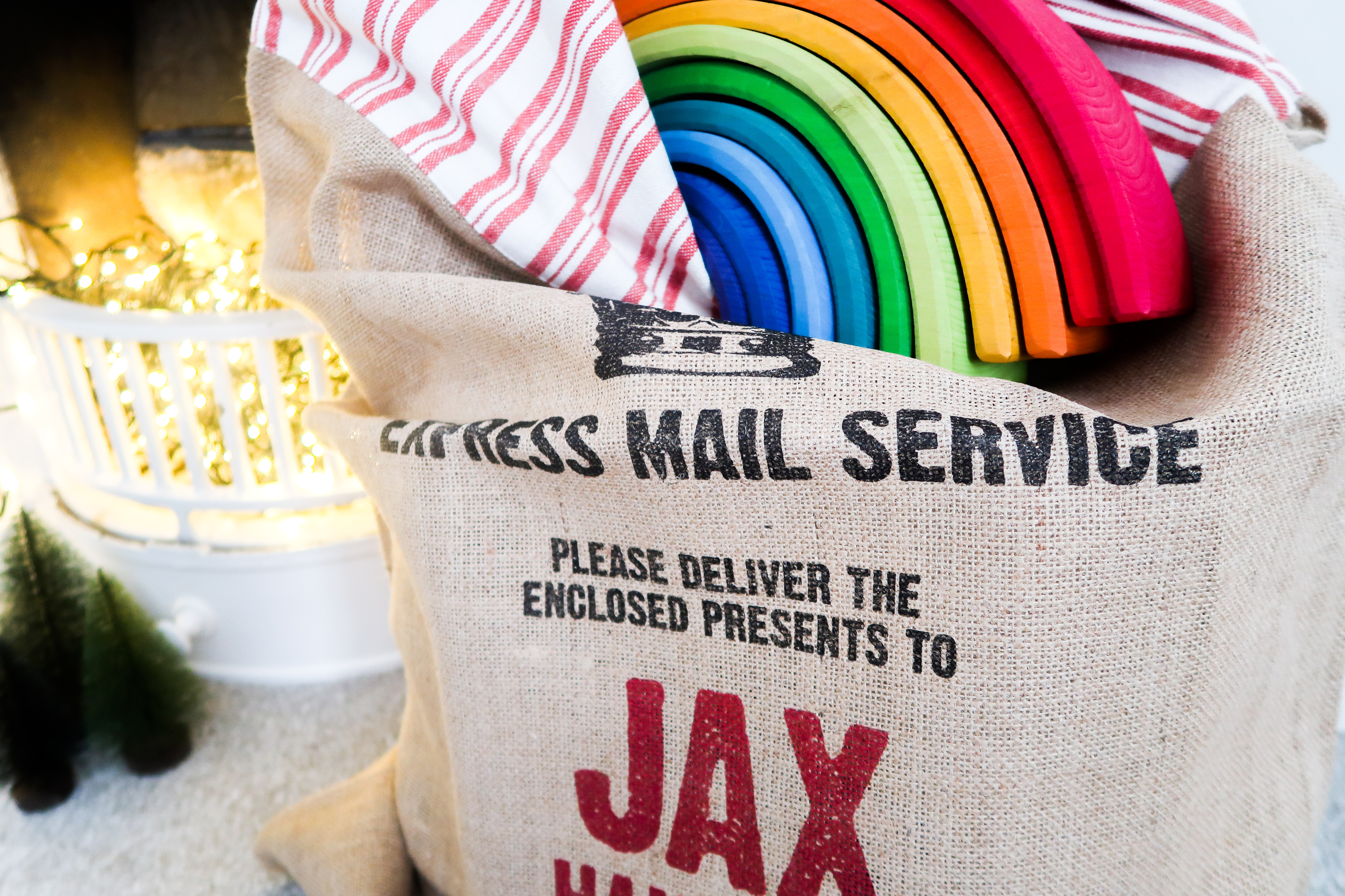 harrow & green personalised hessian christmas sack filled with grimms rainbow and presents next to lights in fireplace